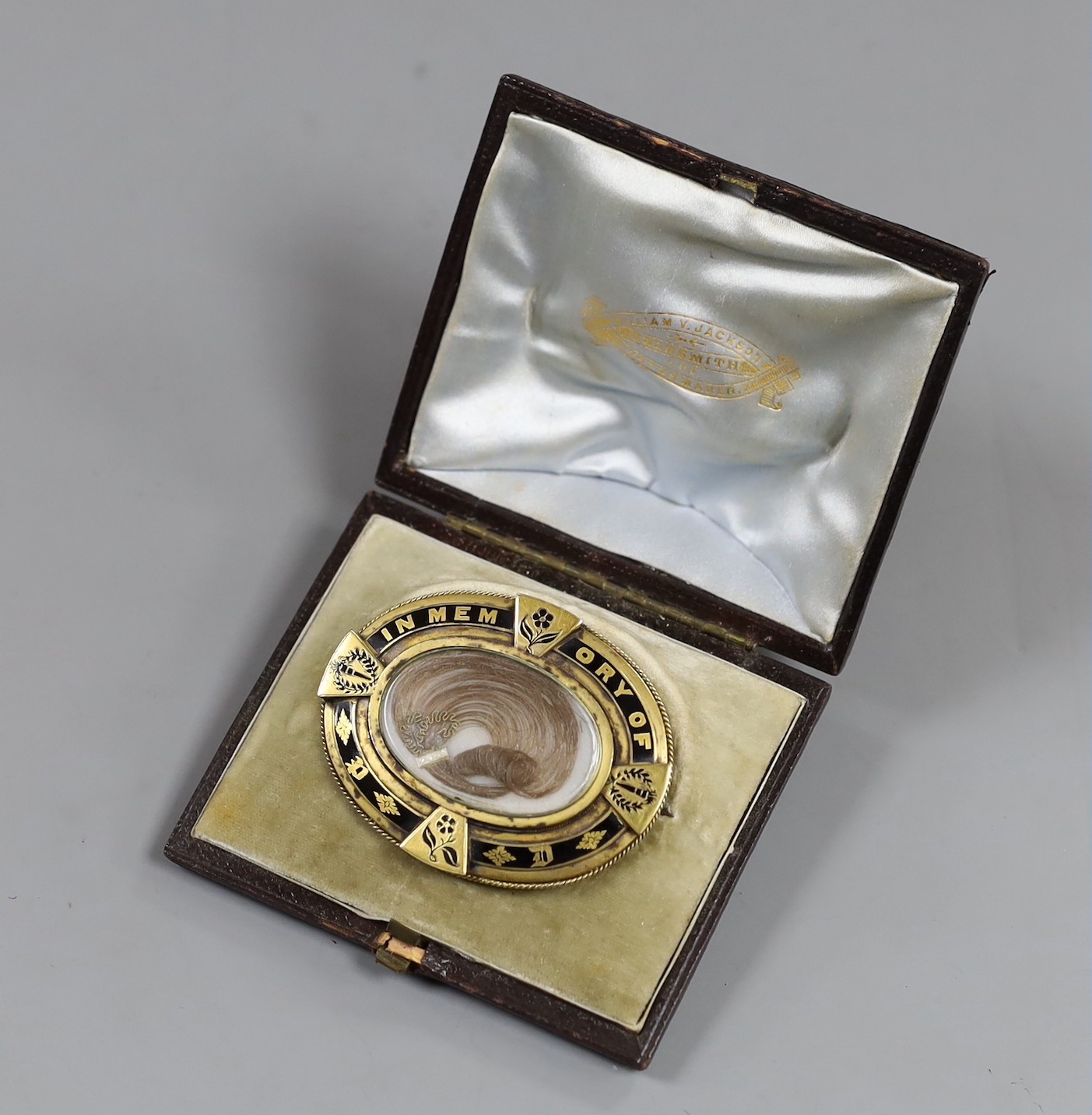 A Victorian yellow metal and black enamel oval memorial brooch, in original box, with plaited hair and inscribed verso 'Peter Dixon Died 14th July 1878 aged 23' with photograph, width 58mm, gross weight 27.9 grams.